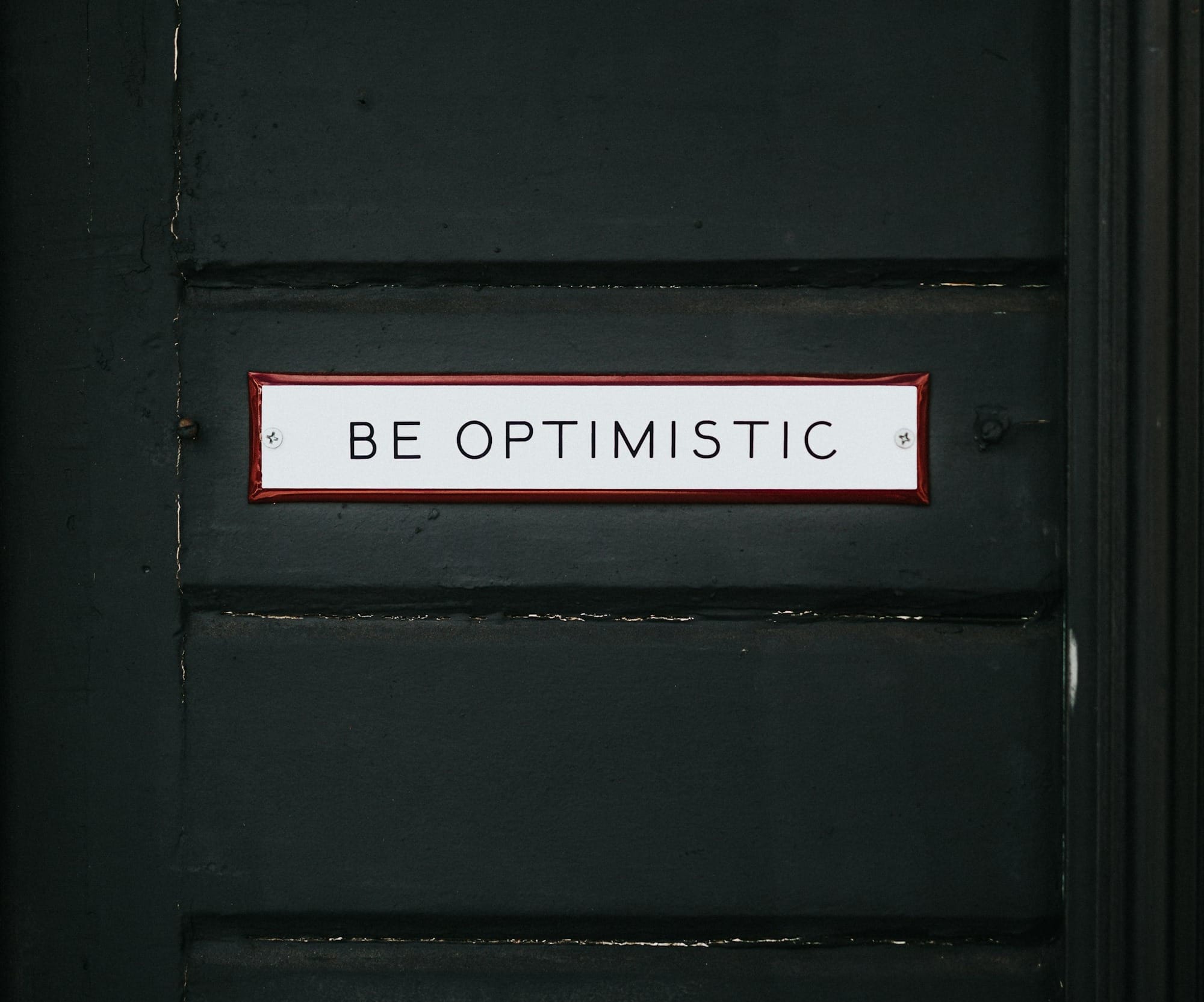 black wooden door with be optimistic text overlay