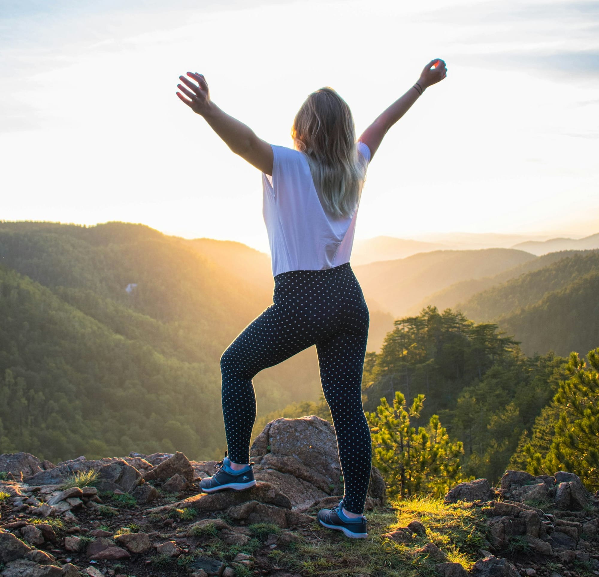 woman in white shirt and black pants standing on rocky mountain during daytime